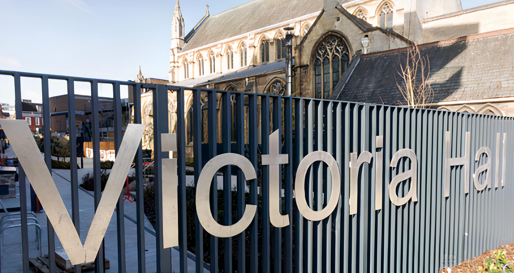 An exterior with a metal fence featuring large letters and a historic church visible in the background at Victoria Hall.