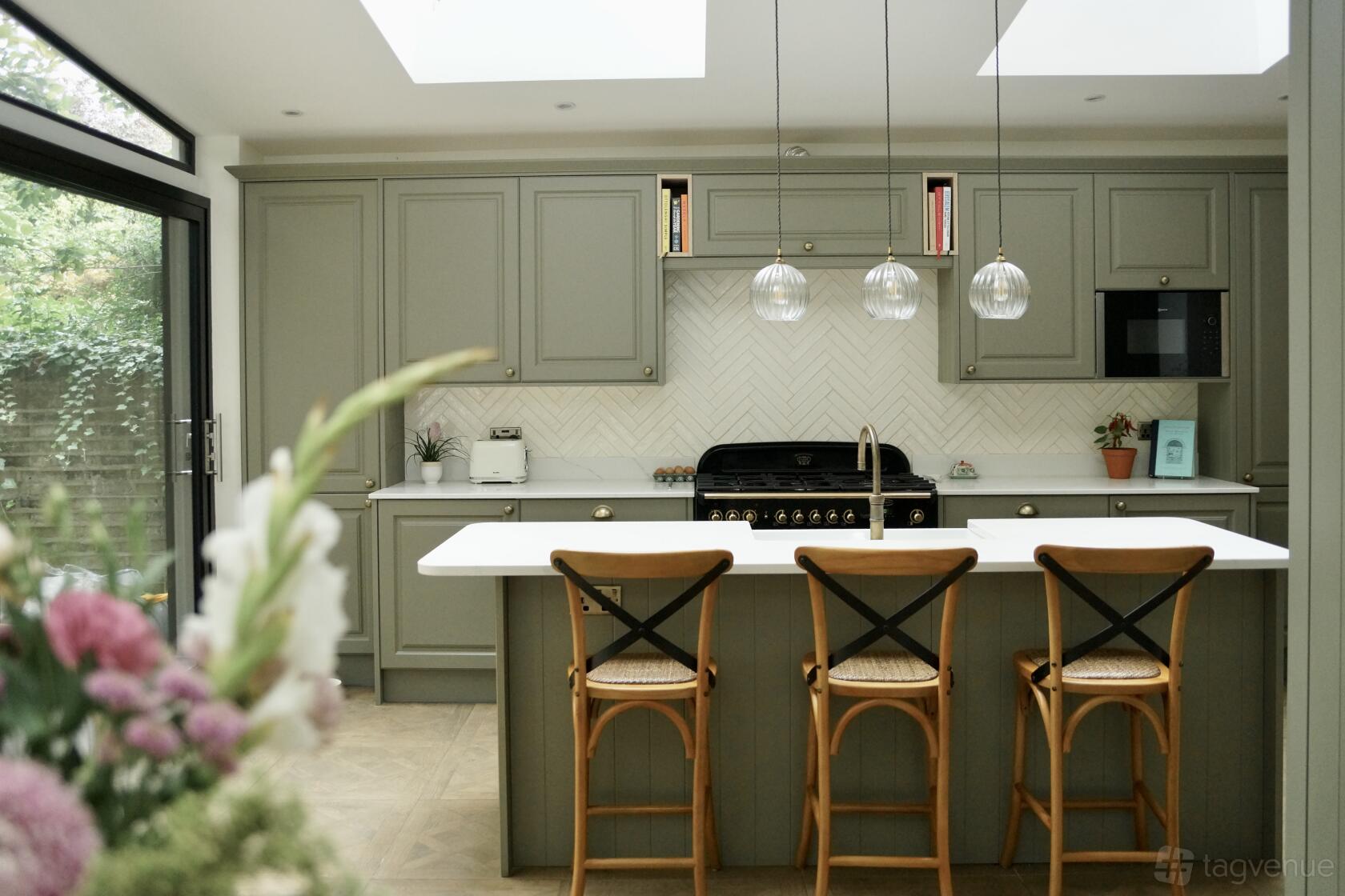 A kitchen with sage green cabinets, herringbone backsplash, pendant lights, and an island with wooden stools at Beautiful Bright Kitchen in Primrose Hill.