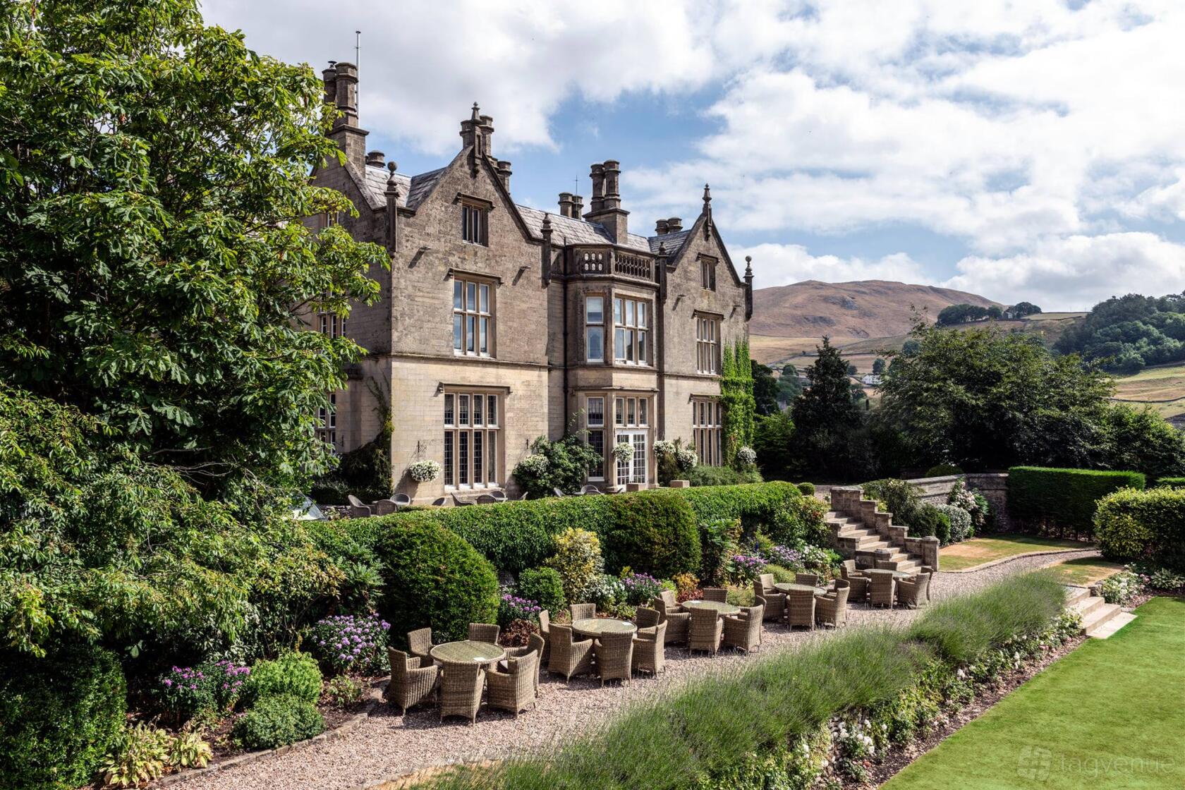 An event venue with manicured gardens, multiple wicker tables and chairs, and a stone manor exterior at Falcon Manor.
