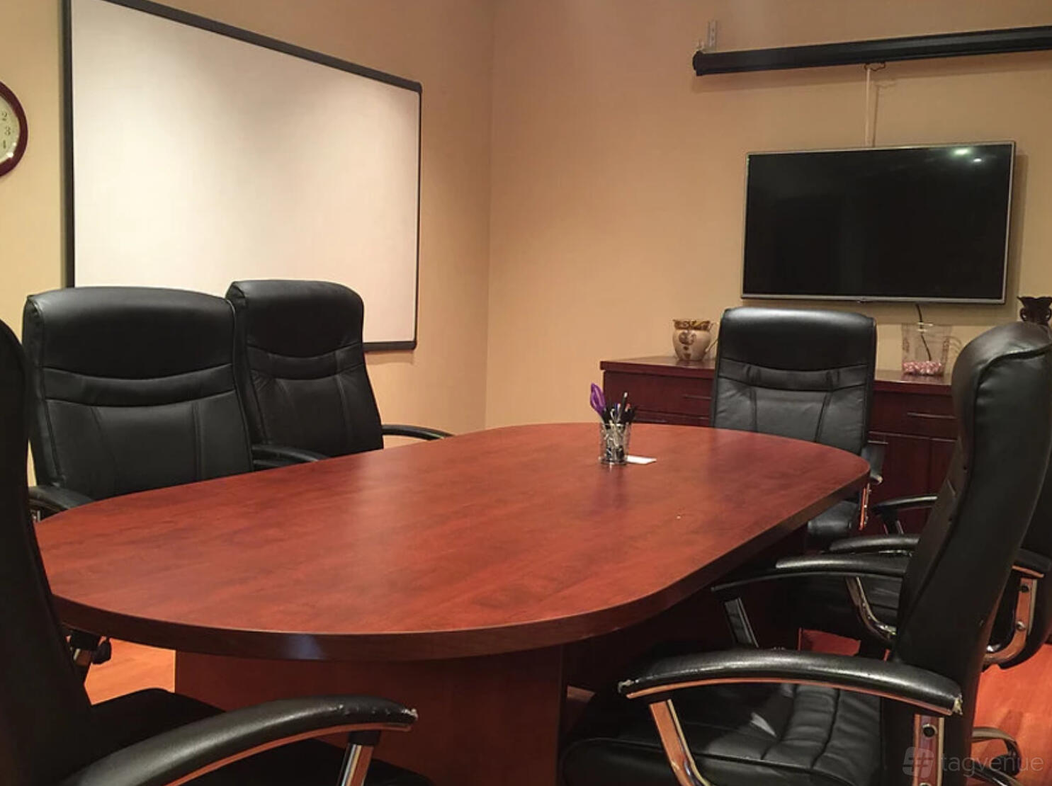 A recording studio conference room with a wooden oval table, leather chairs, and presentation screen at McPhail Studios.