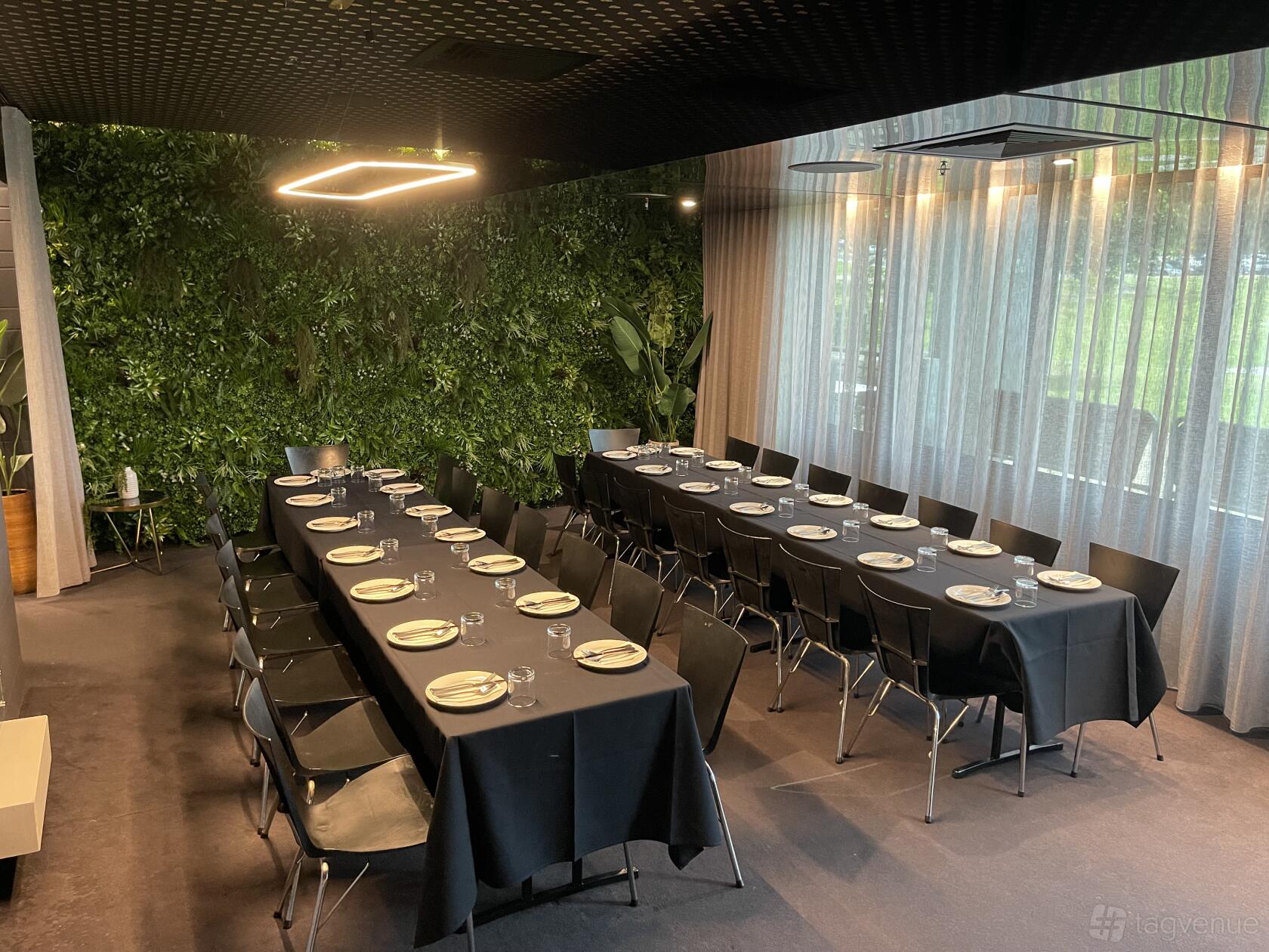 A lounge in a restaurant with floor-to-ceiling sheer curtains, a vertical garden wall, and banquet tables at Switch Lifestyle.