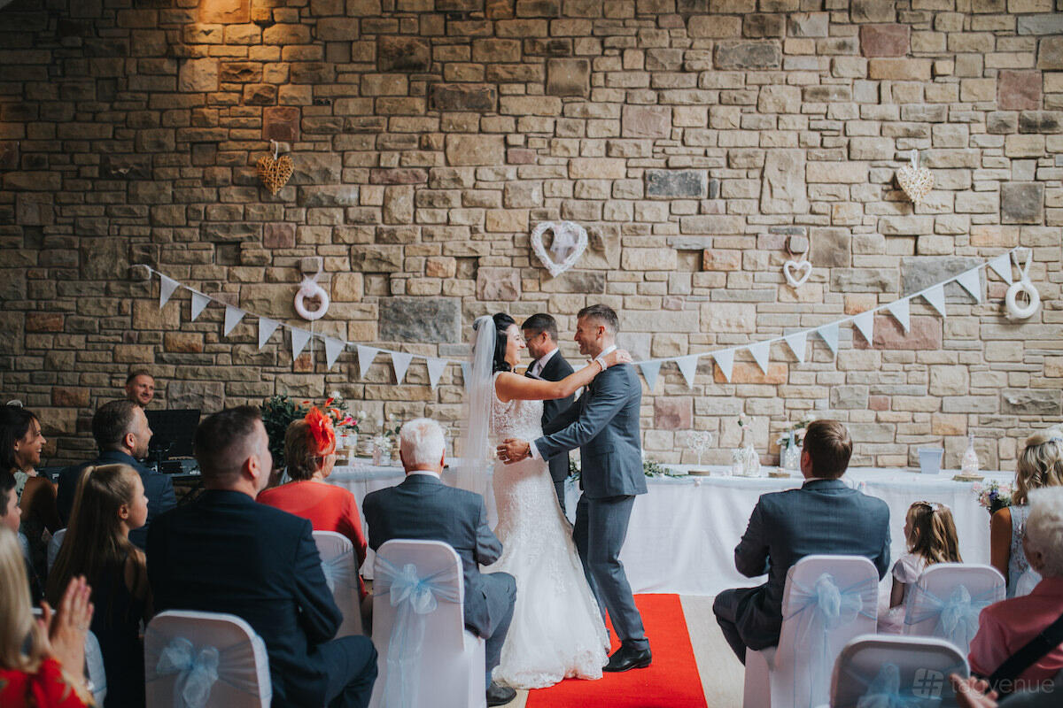 An event hall with stone walls, bunting decorations, and white chair covers at Marsh Farm Hall.