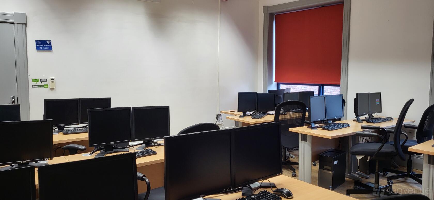 A training room with computer workstations, black chairs, and a red window shade at Nexus Human Training Centre.