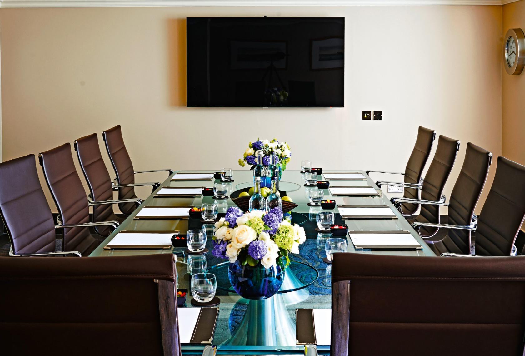 A hotel meeting room with a glass conference table, leather chairs, and floral centerpieces at Radisson Blu Hotel, London South Kensington.