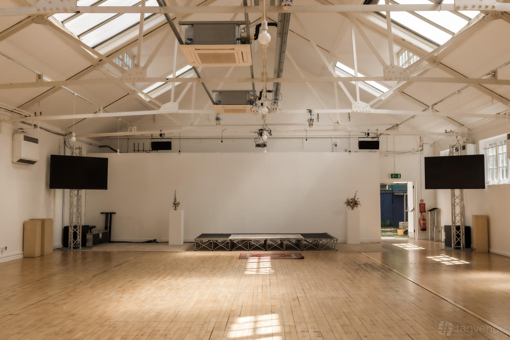 An event venue with high ceilings, exposed beams, skylights, and a small stage at 1-3 Coborn Street.