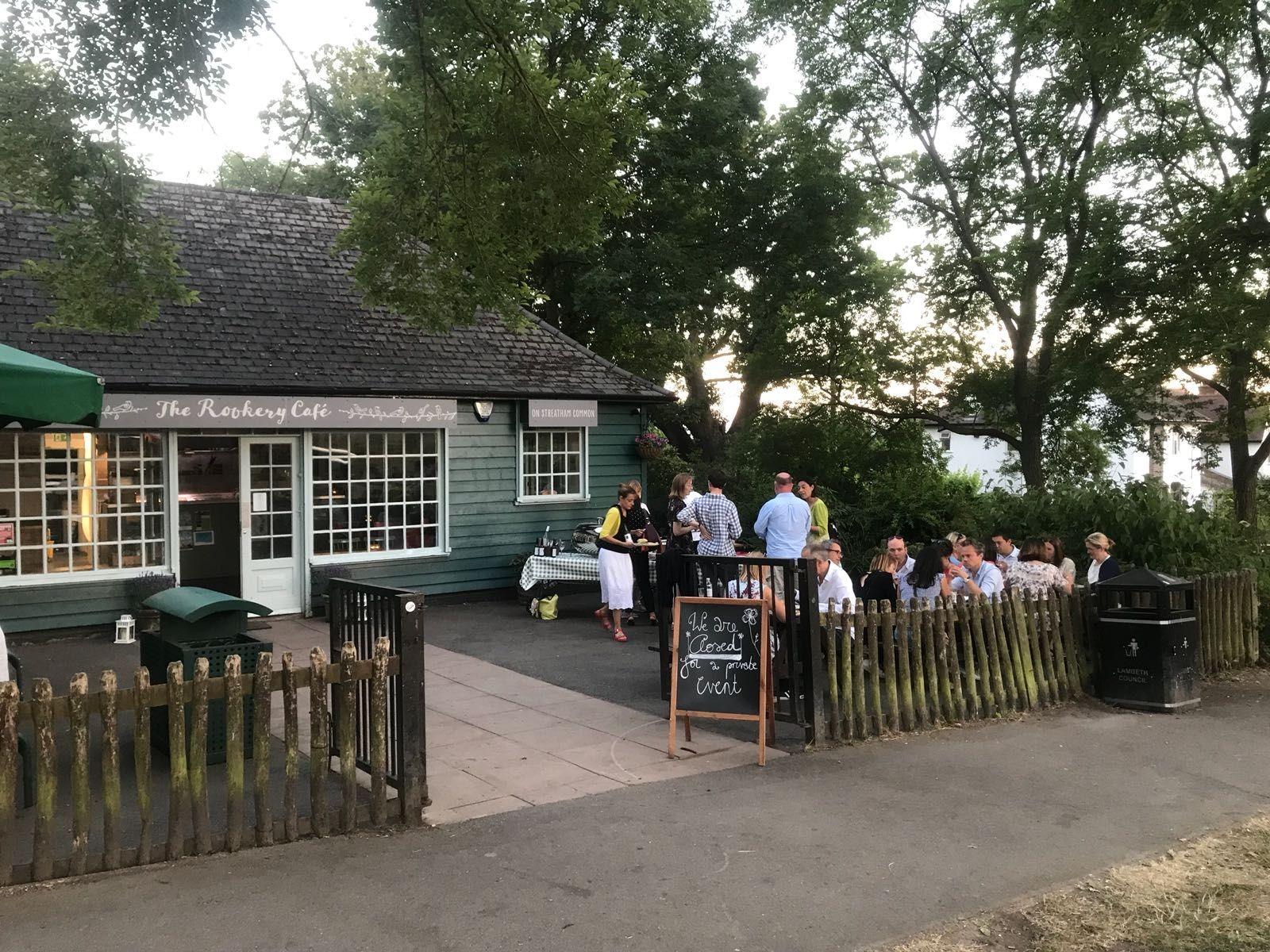 A cafe with outdoor seating under large trees and rustic wooden fencing at The Rookery Cafe.