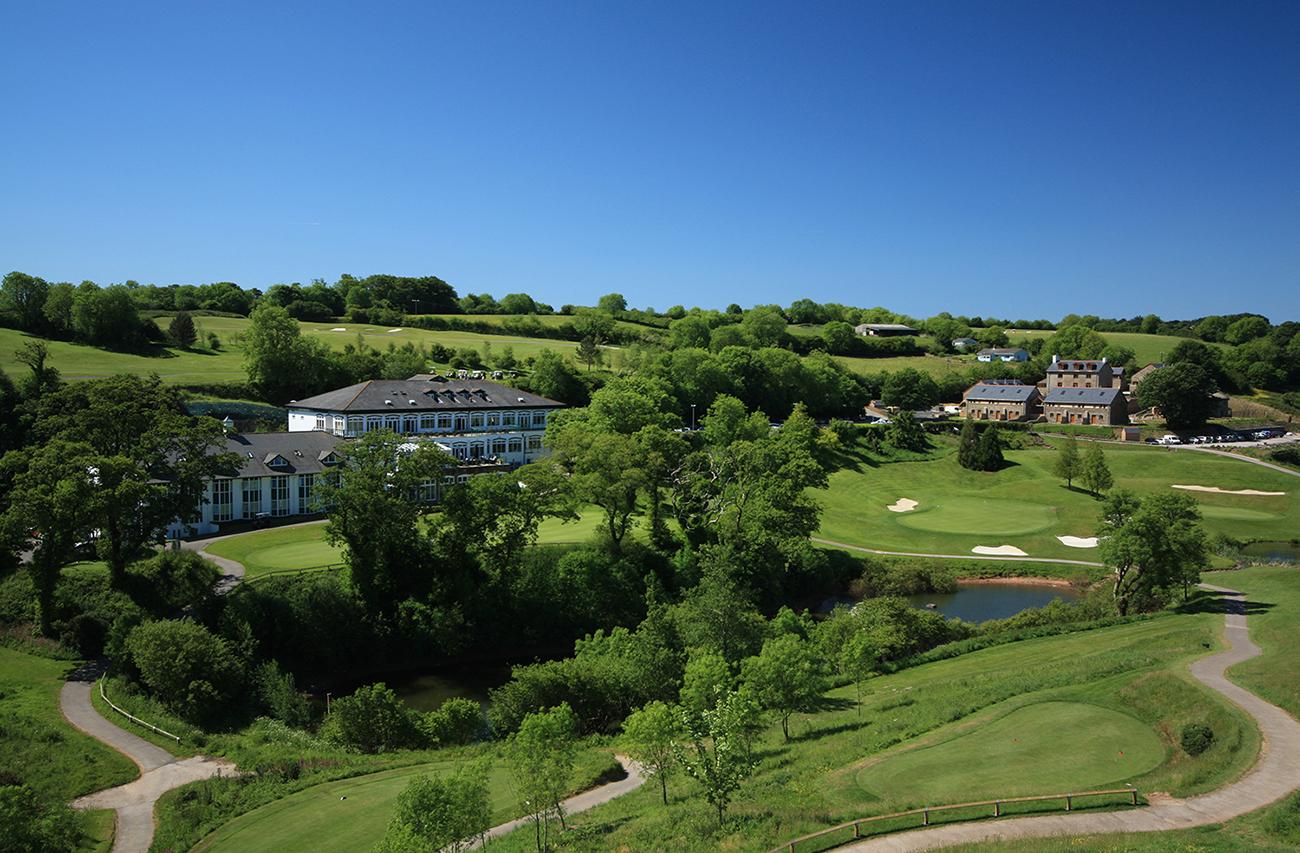 A hotel surrounded by green rolling golf courses, mature trees, and a small pond at The Dartmouth Hotel, Golf & Spa.