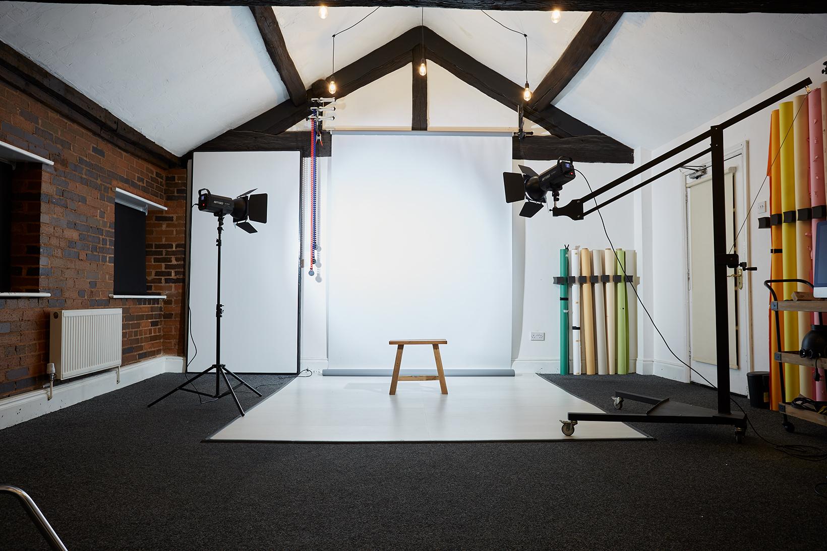 A photo studio with backdrop rolls, lighting equipment, exposed beams, and a wooden stool at Black Star Studio.