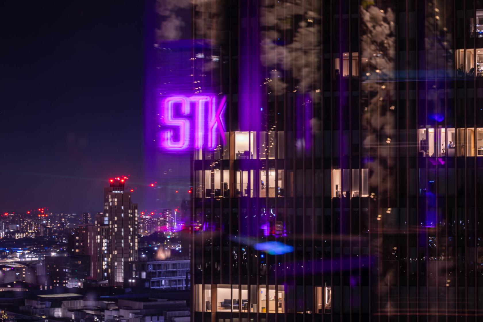 A restaurant high above the city with a glowing STK rooftop sign and surrounding night skyline at STK Rooftop - Stratford.