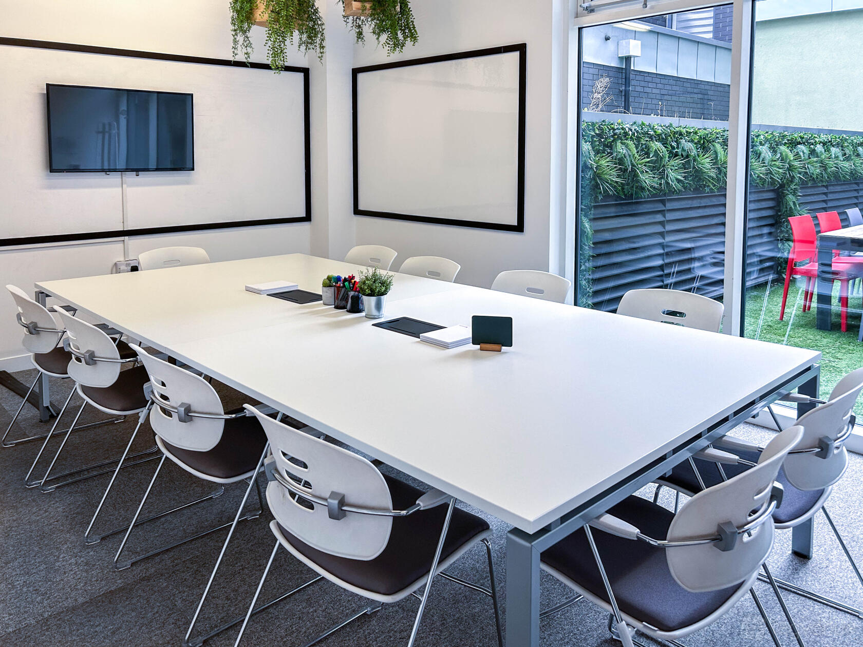 A meeting room with a large white conference table, wall-mounted TV, whiteboards, and glass doors at Moneypenny Workhub.