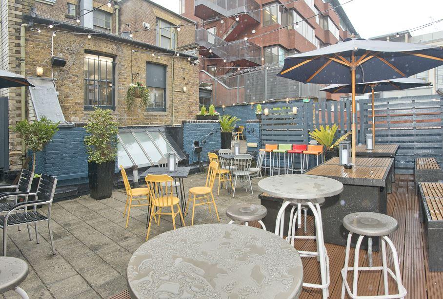 An outdoor pub terrace with round tables, mixed chairs, umbrellas, and potted plants at Hop Poles.