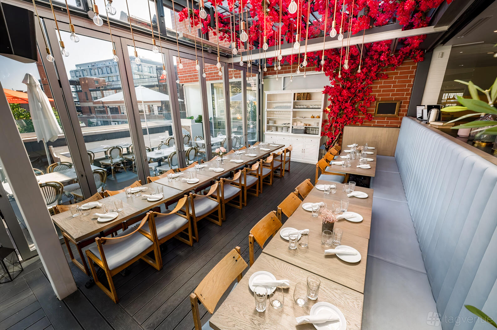 A restaurant with floor-to-ceiling windows, wood tables, and red floral ceiling decor at Nodo Liberty.