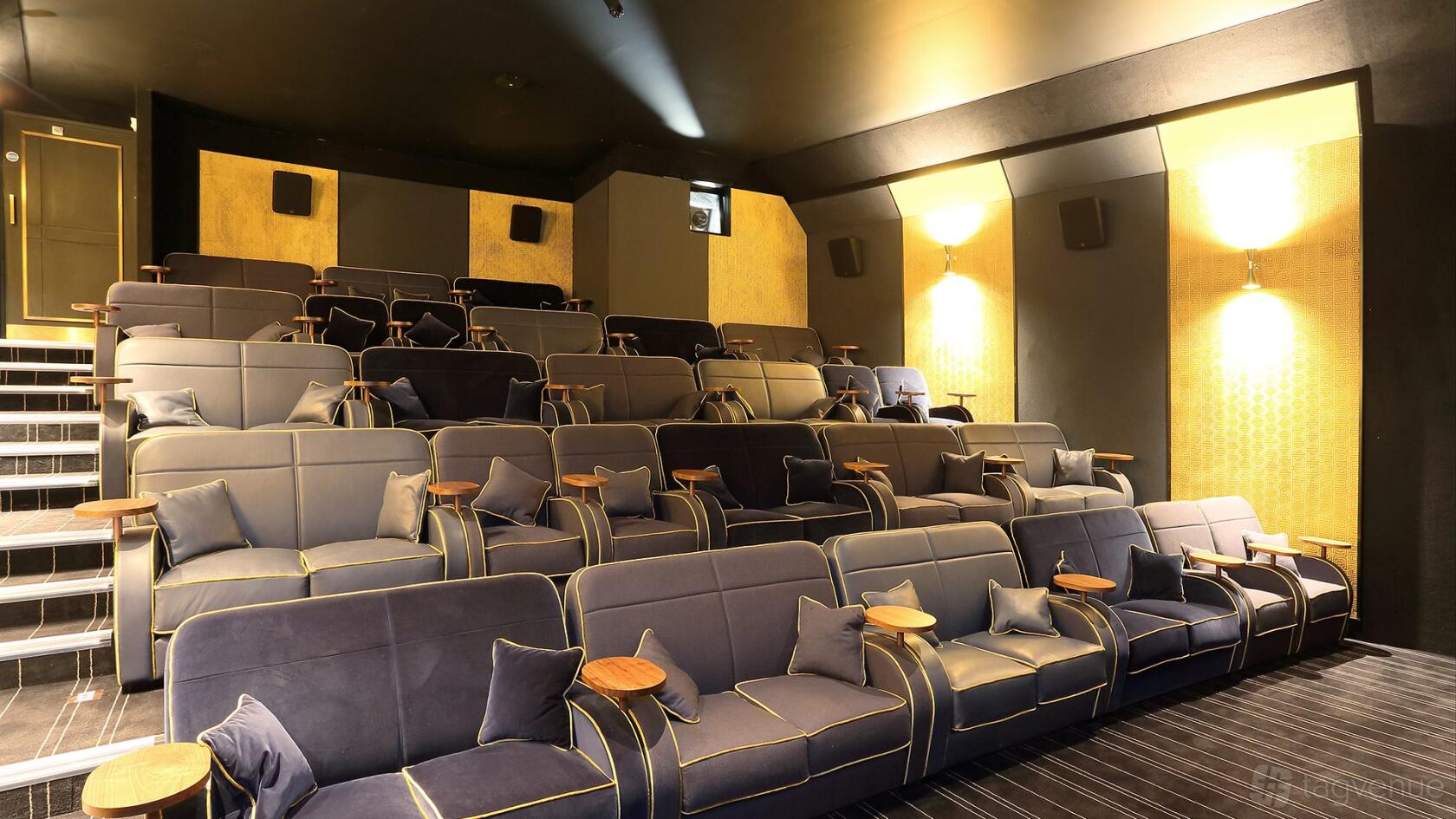 A screening room with tiered plush sofas, small side tables, and gold-accented walls at Everyman Muswell Hill.