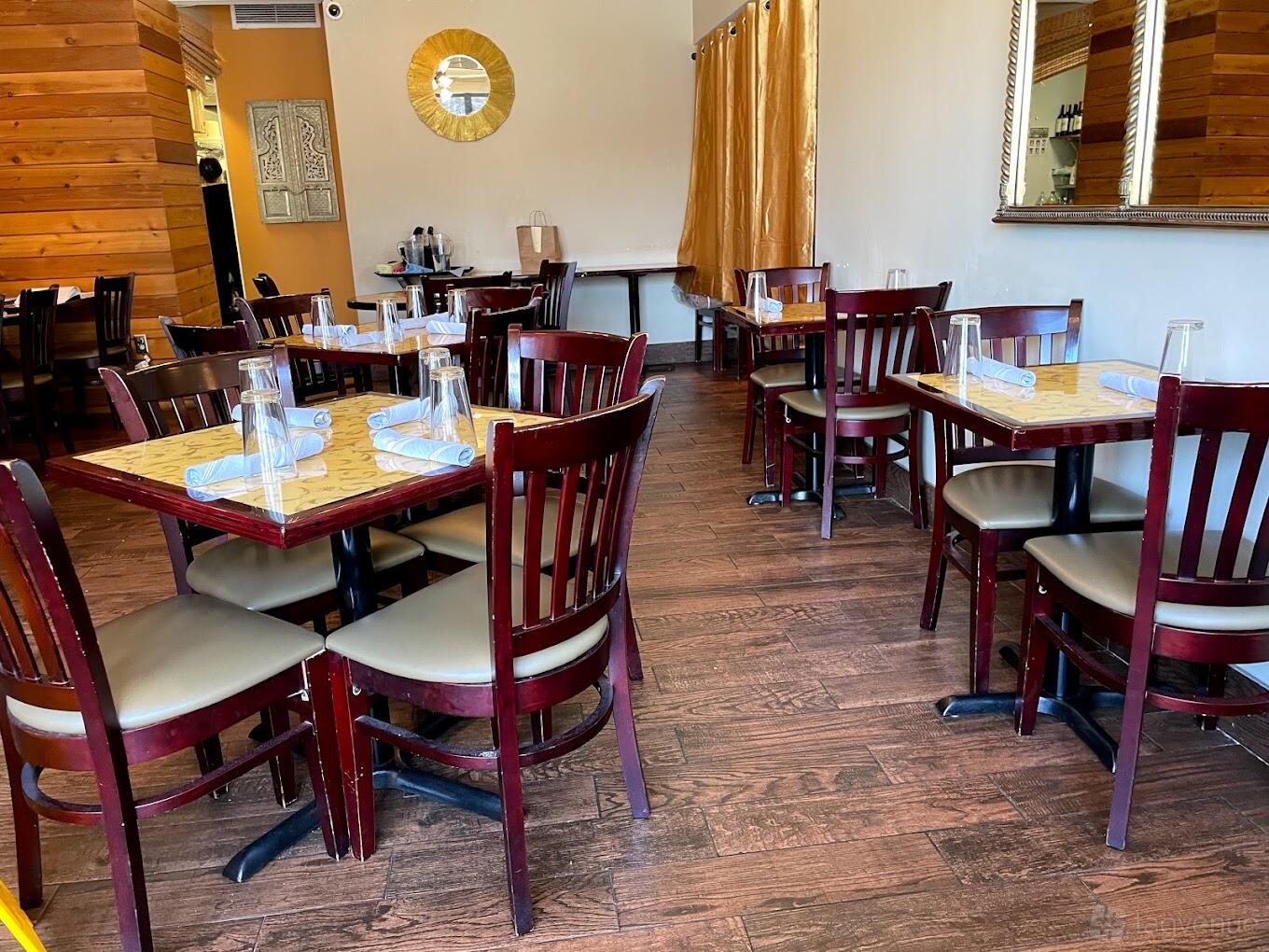 A restaurant dining area with wooden floors, square tables set with glassware and napkins at Spice Kraft Indian Bistro Alexandria.