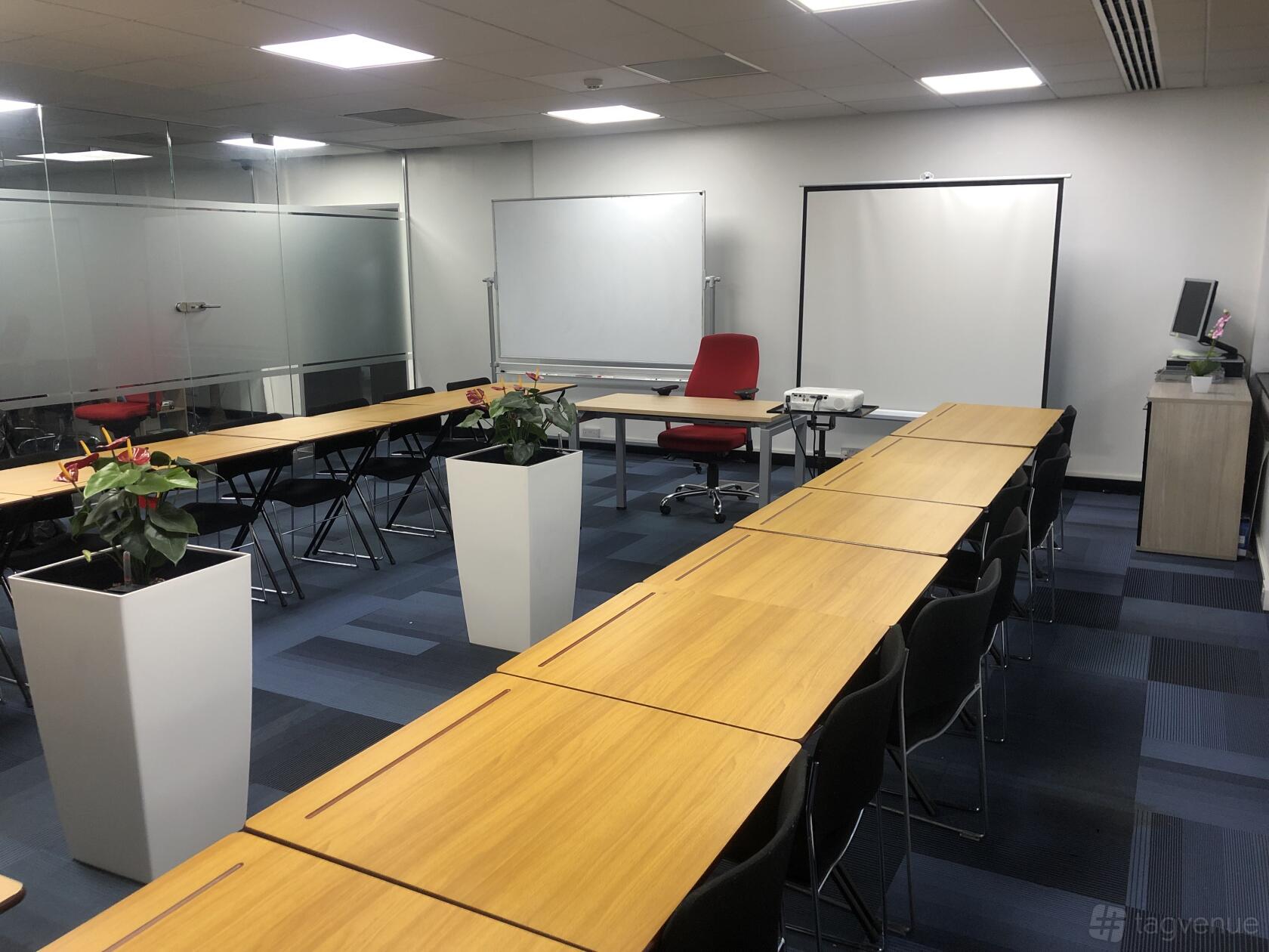 A conference centre with U-shaped wooden tables, black chairs, and potted plants at Stratford.