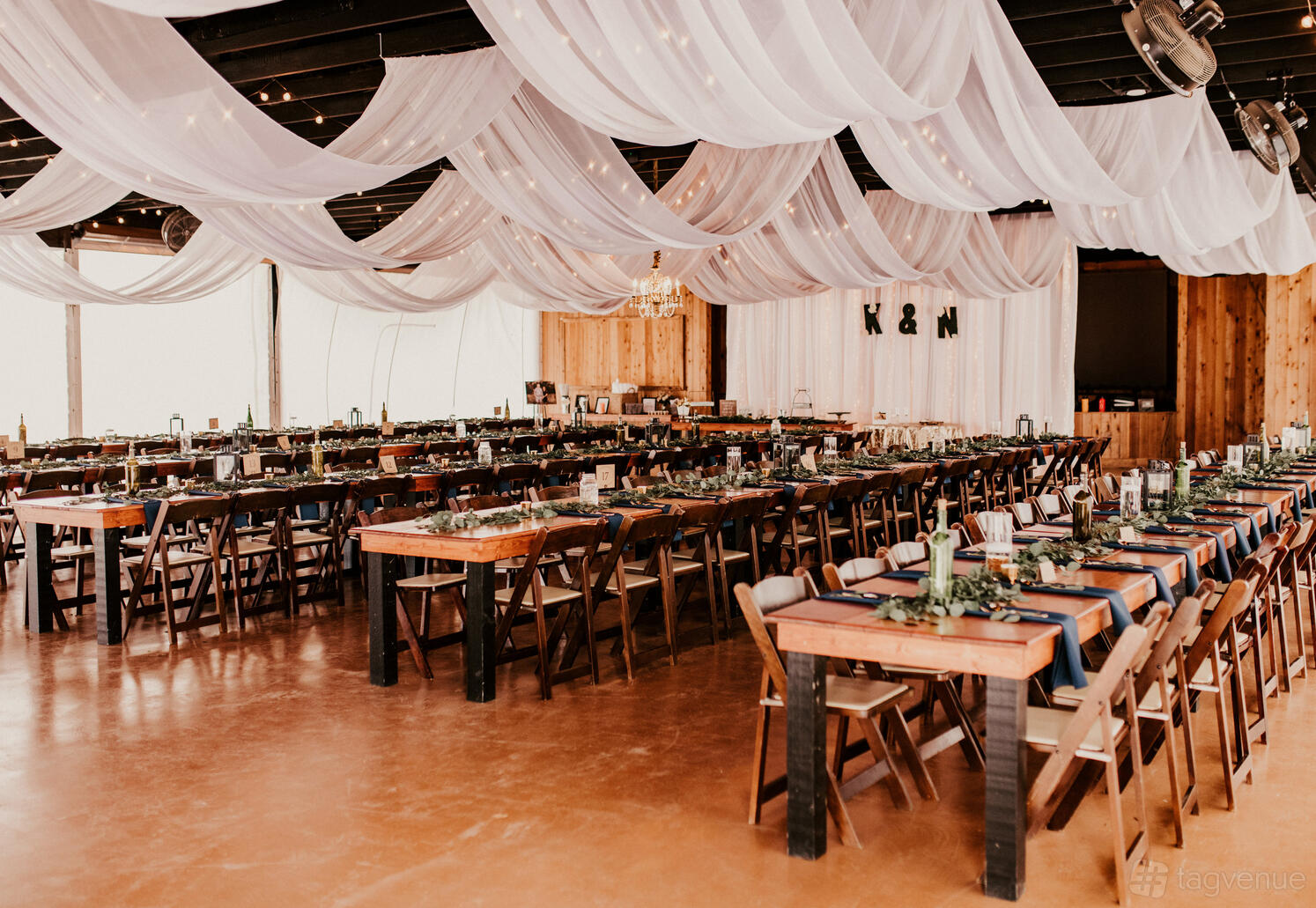 An event venue with draped white fabric ceiling, wooden tables with navy runners, and greenery at Bentwood Texas.