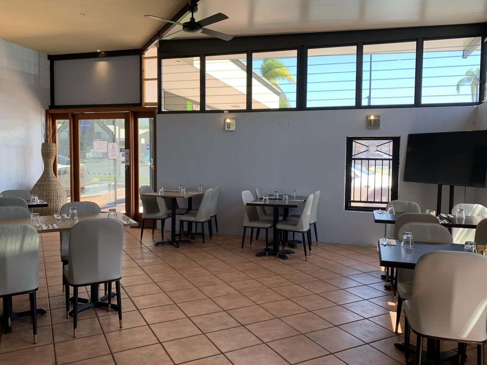 A dining room with tiled floors, light gray chairs, large windows, and several set tables at Portabella Restaurant.