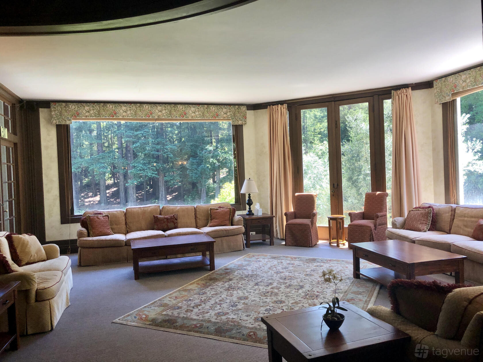 An event venue living room with large windows, forest views, plush sofas, and wooden coffee tables at Ralston White Retreat.