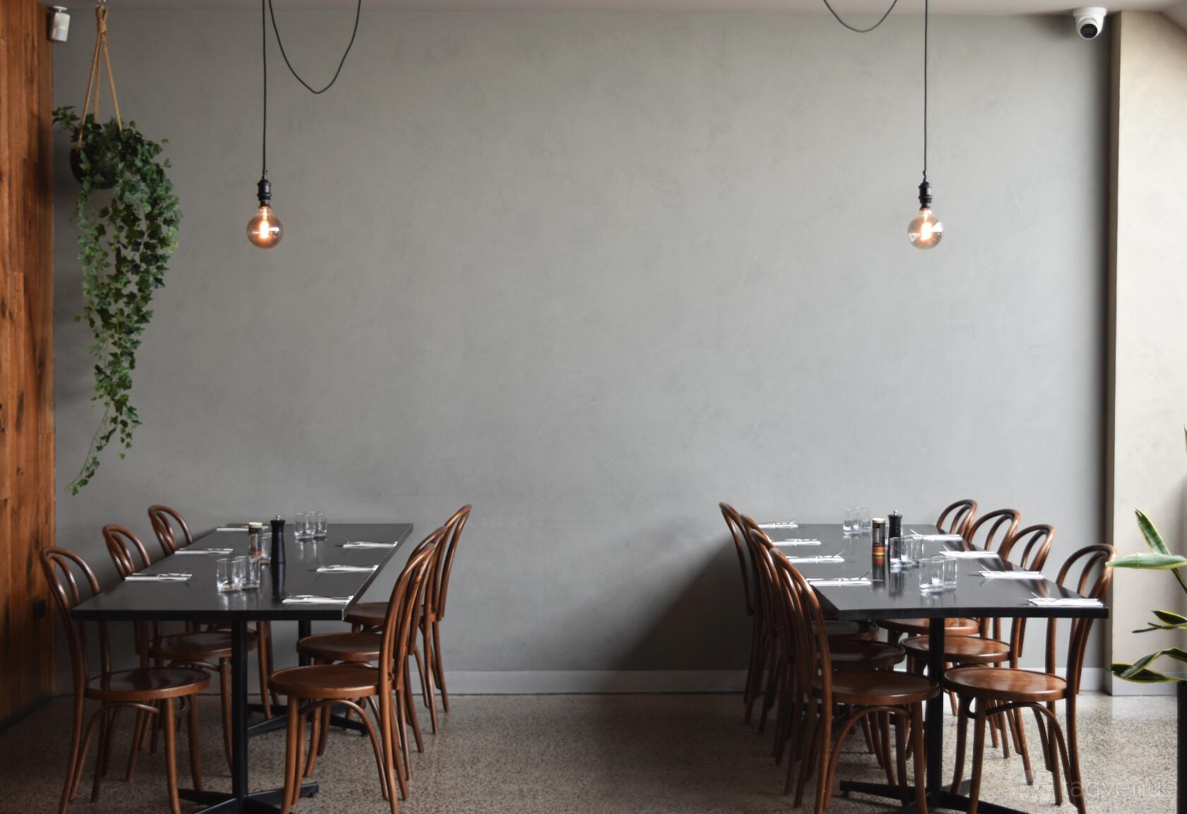 An event space in a restaurant with long tables, wooden chairs, hanging bulbs, and a bare concrete wall at Dawson.