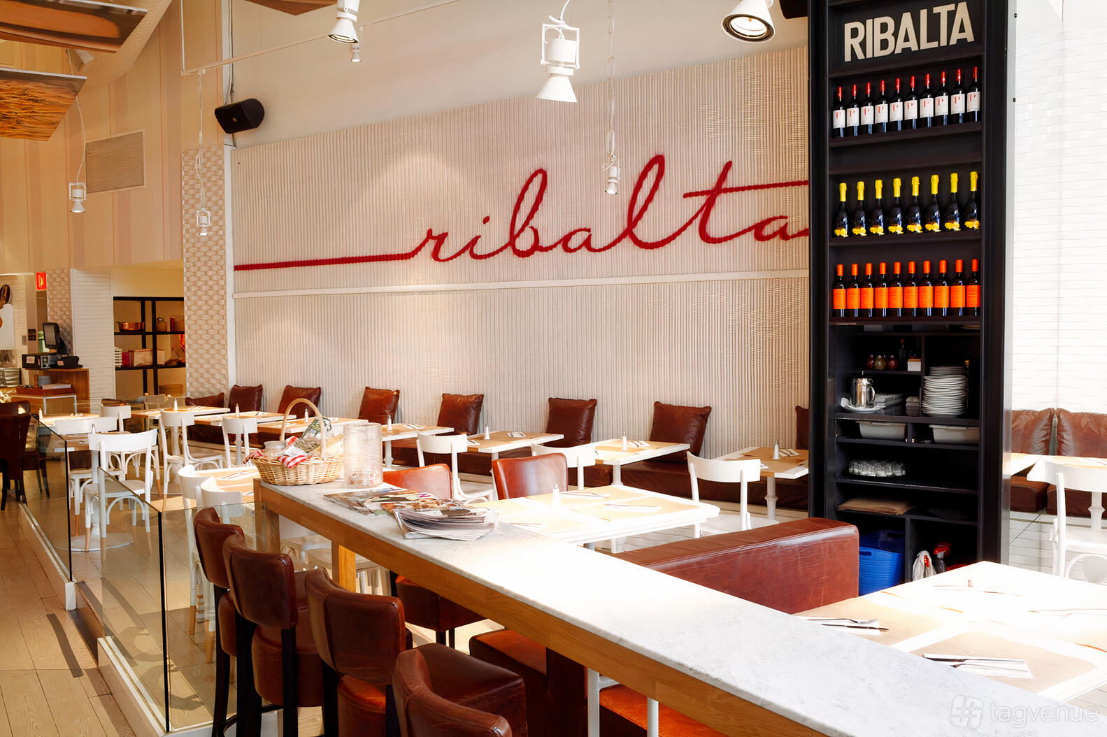 A pizzeria with brown leather chairs, white tables, and a wall of wine bottles at Ribalta.