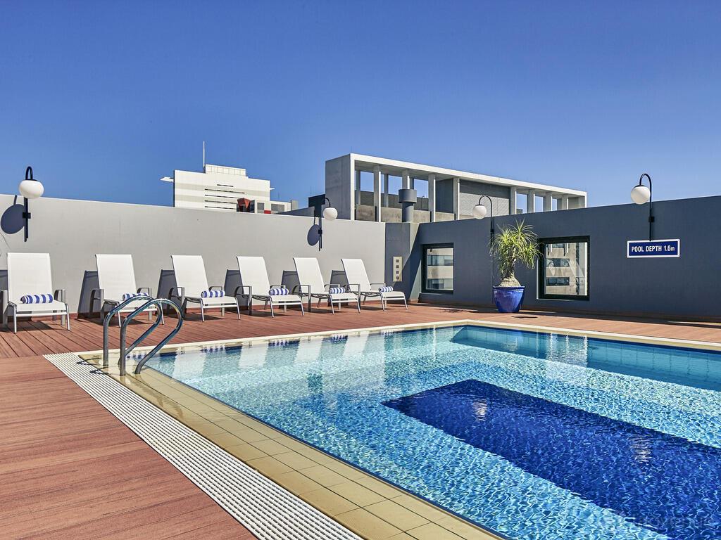 A hotel rooftop with an outdoor swimming pool, poolside loungers, and potted plants at Mercure Perth.
