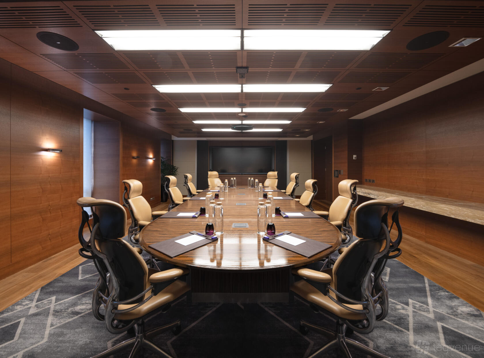 A boardroom with a large oval wooden table, ergonomic chairs, and wood-paneled walls at Sofitel Sydney Wentworth.