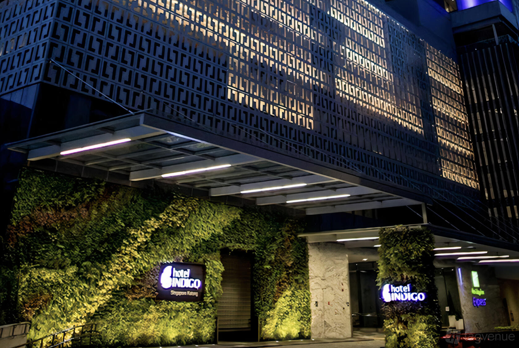 A hotel exterior with a patterned facade, greenery wall, and illuminated signage at Hotel Indigo Singapore Katong.