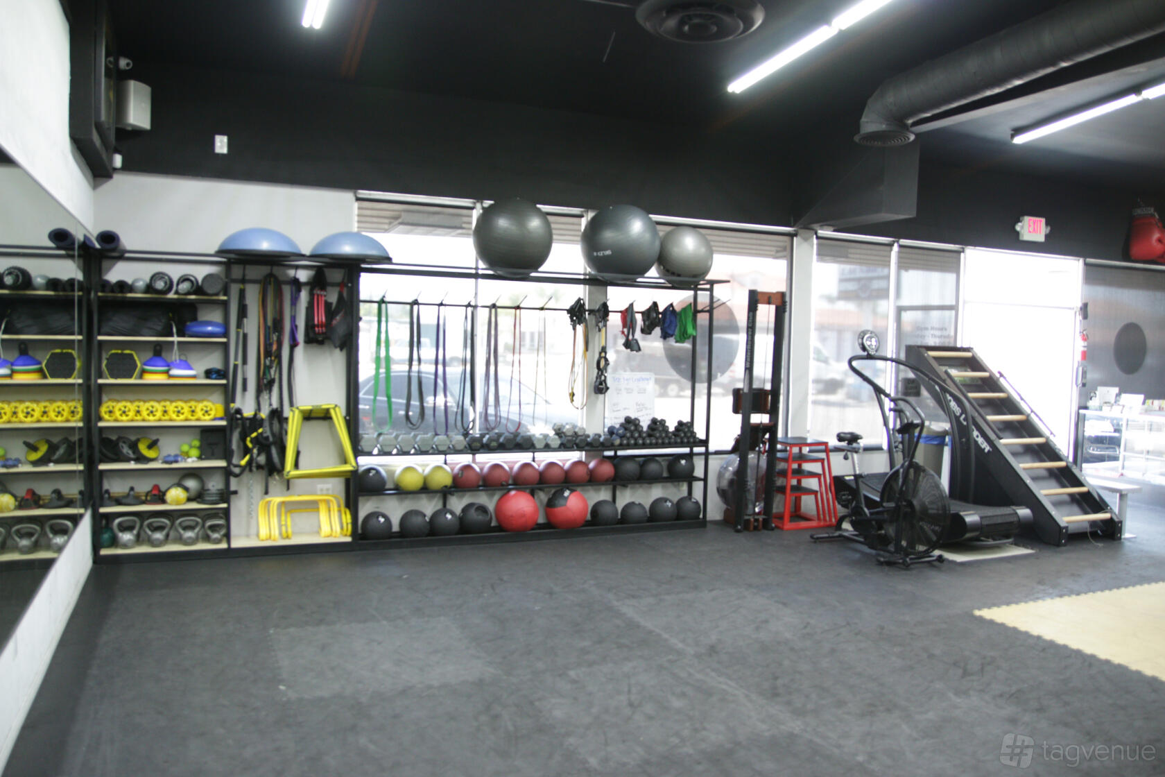 A sports club studio with exercise balls, resistance bands, and free weights organized on wall racks at BomberSquad Academy.