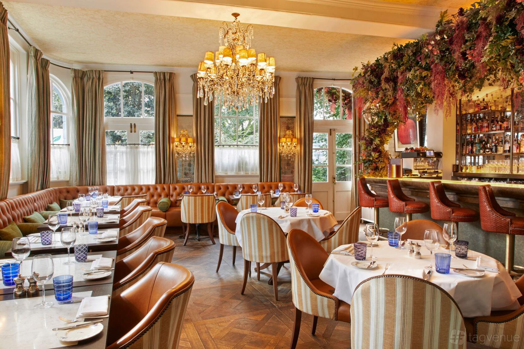 A restaurant with a crystal chandelier, floral decor, tan leather seating, and round tables at No. Fifty Cheyne.