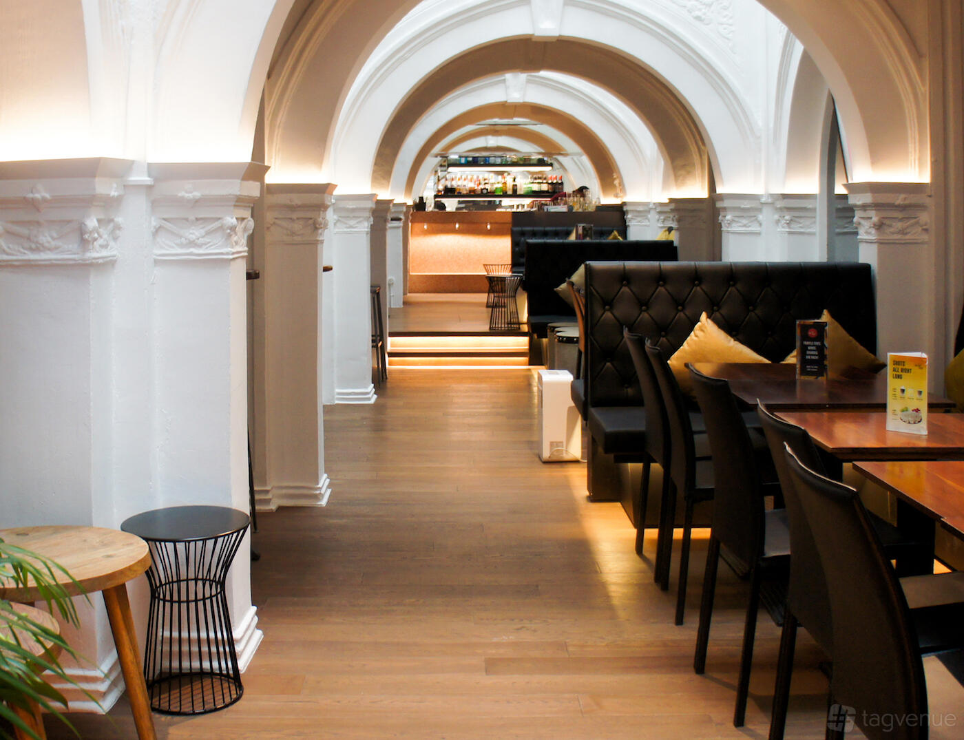 A lounge in a restaurant with tufted black booth seating, arched white ceilings, and wooden floors at Acid Bar.