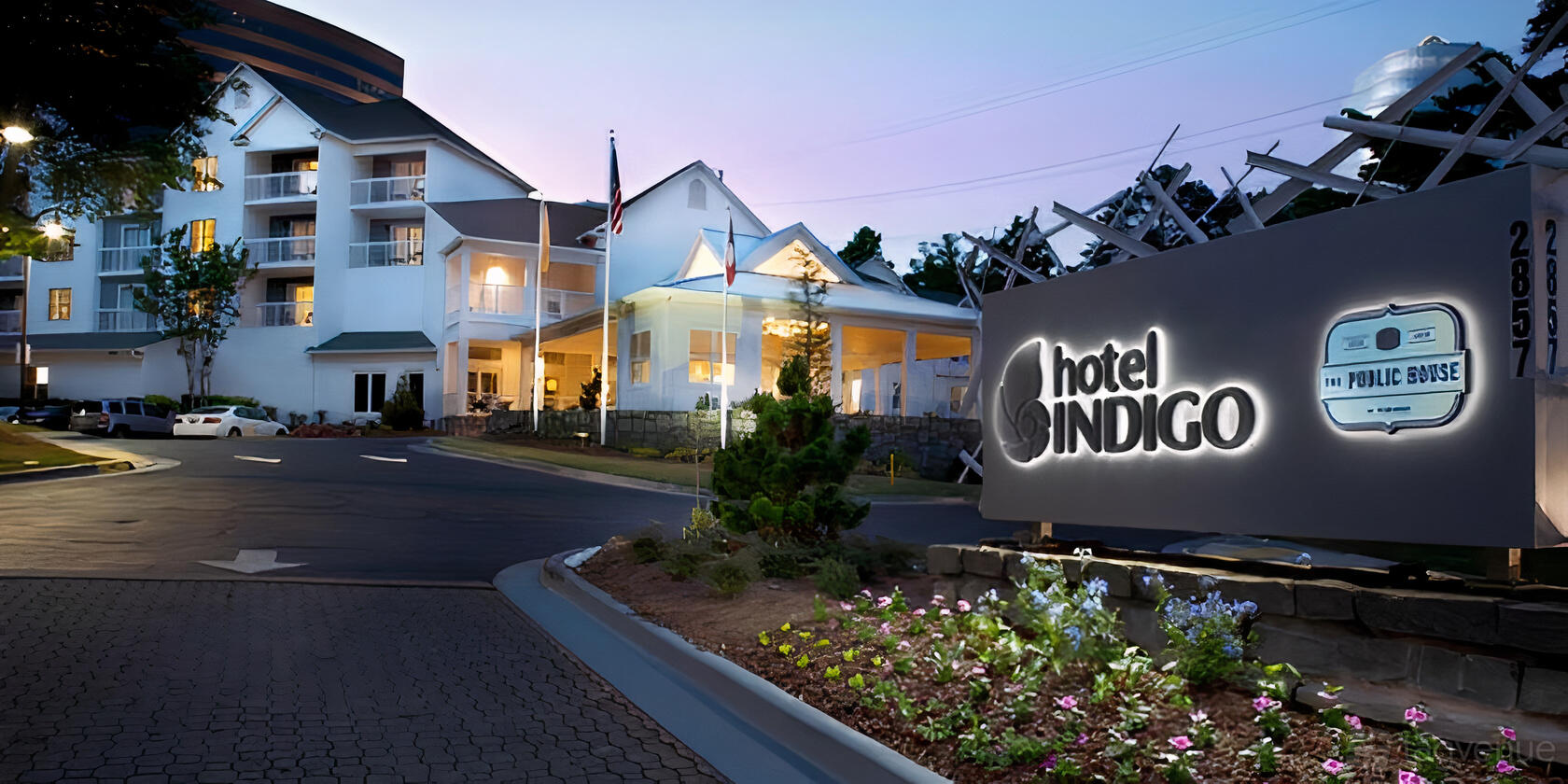 A hotel with a covered entrance, white facade, and illuminated signage at Hotel Indigo Vinings.