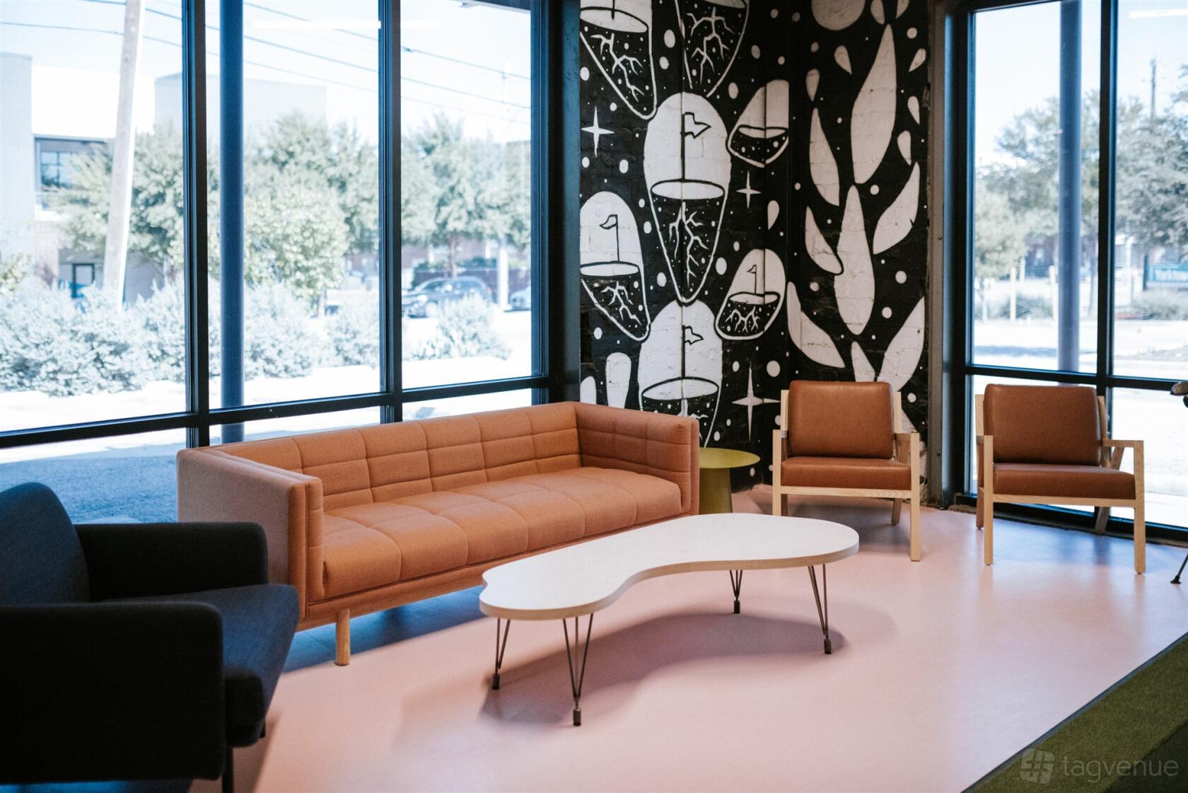 An event space with floor-to-ceiling windows, a mural wall, and modern lounge seating at Another Round.