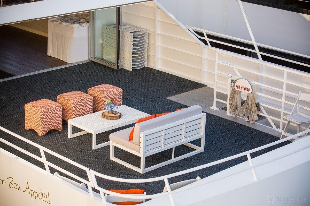 A yacht with an outdoor deck featuring lounge seating, ottomans, a low table, and nautical railings at Merlot Yacht.