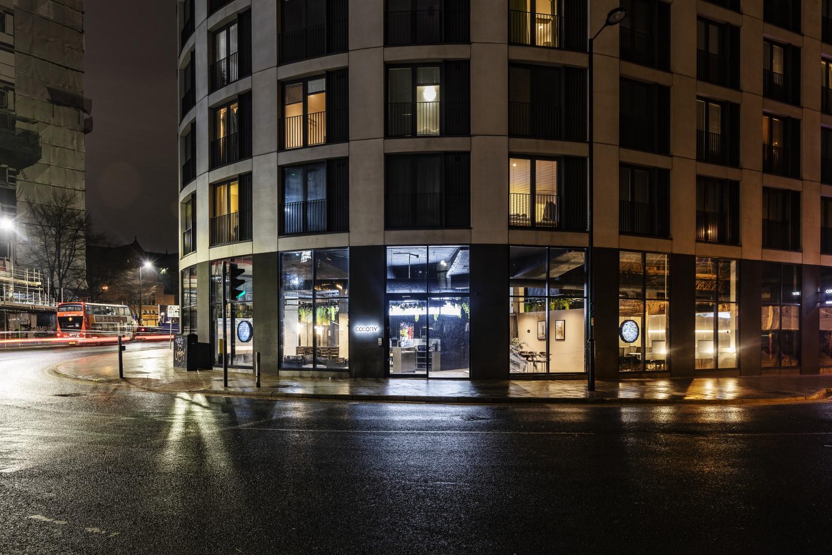 A coworking space with floor-to-ceiling windows and visible interior lighting at Colony Piccadilly.