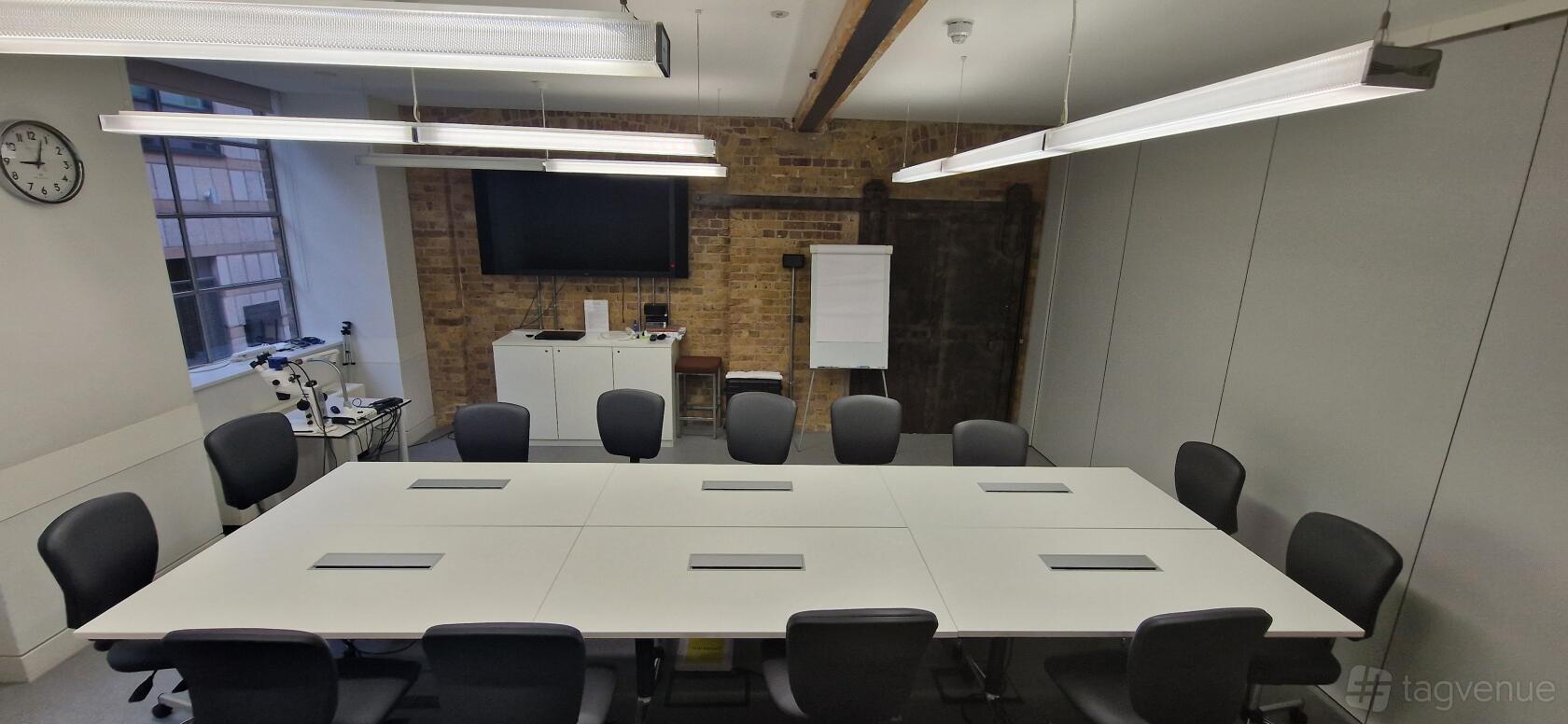 A meeting room with white conference tables, black chairs, exposed brick wall, and a wall-mounted screen at The Royal College of Ophthalmologists.