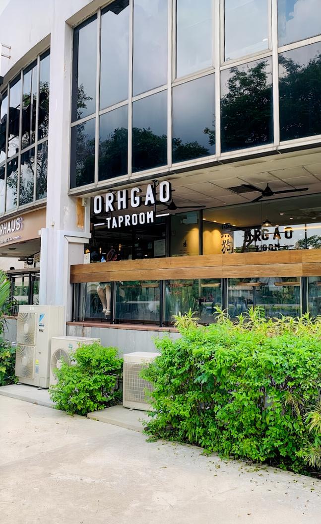 A pub with large glass windows, wooden bar seating, and visible signage at Orh Gao Taproom Craft Beer Bar.
