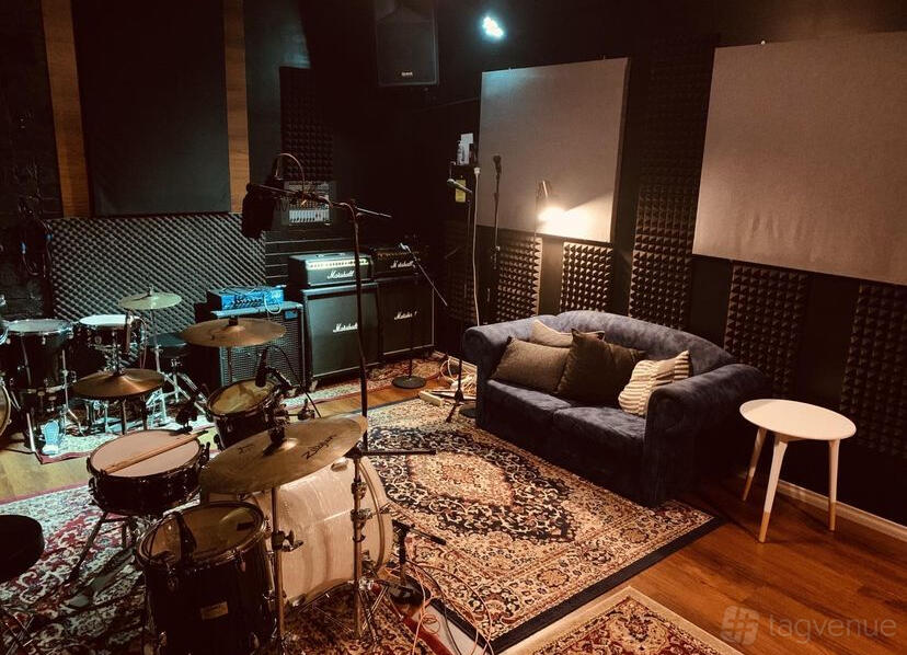 A rehearsal room with drum kit, guitar amps, soundproofed walls, a blue sofa, and patterned rugs at Bayside Rehearsal Studios.