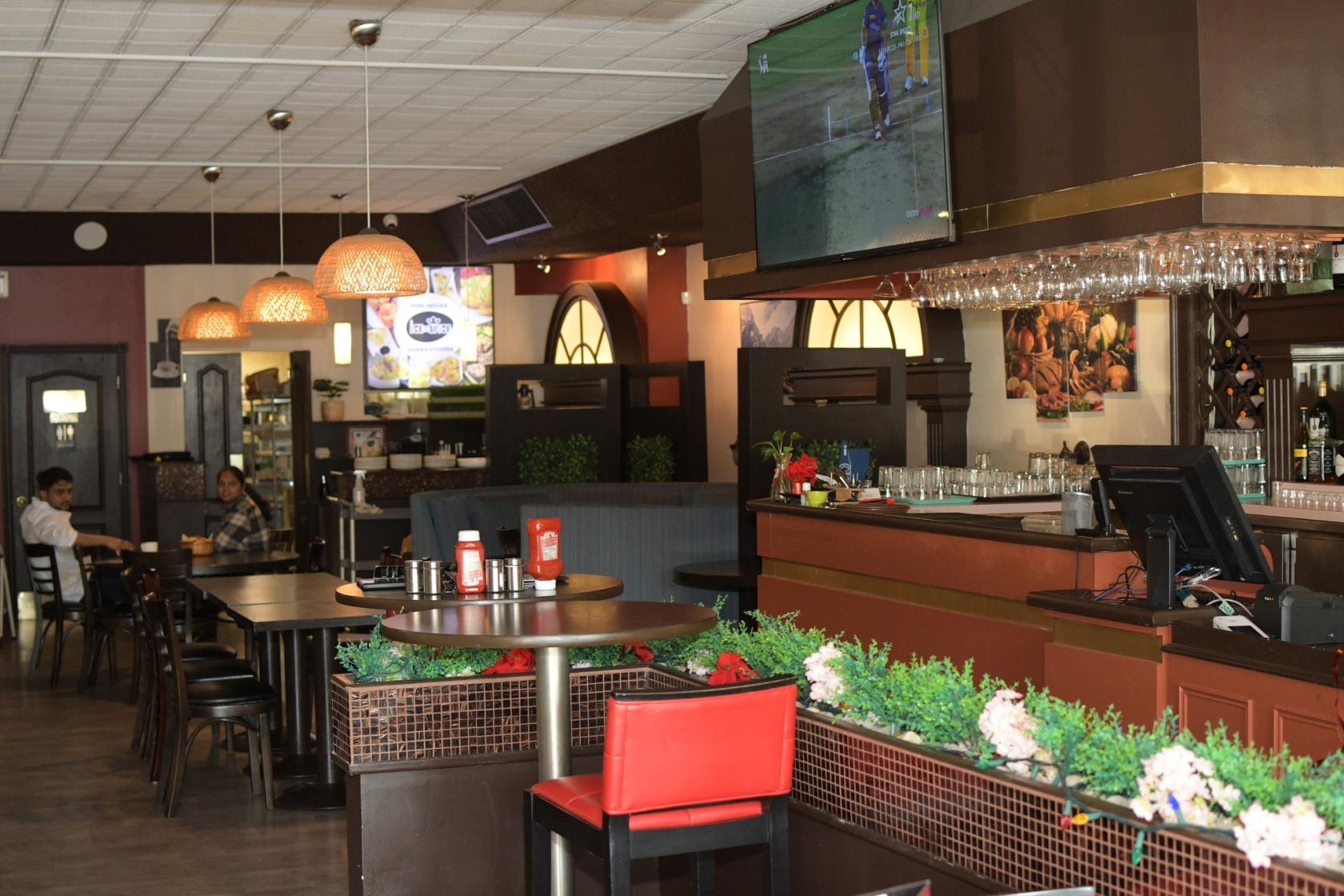 A restaurant dining area with wooden tables, hanging pendant lights, a bar counter, and wall-mounted TV at Ice N Spice.