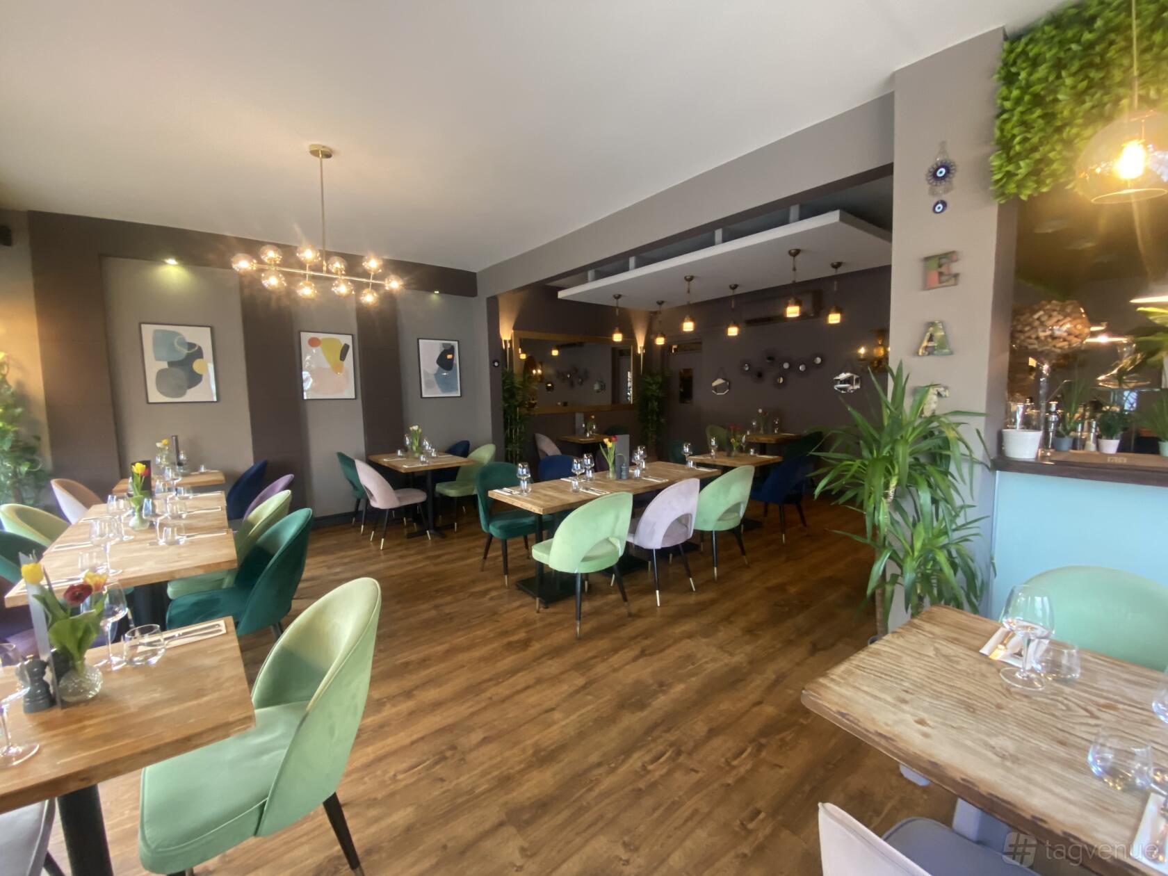 A restaurant with wooden floors, colorful upholstered chairs, wall art, and hanging light fixtures at Mosaic Kitchen.