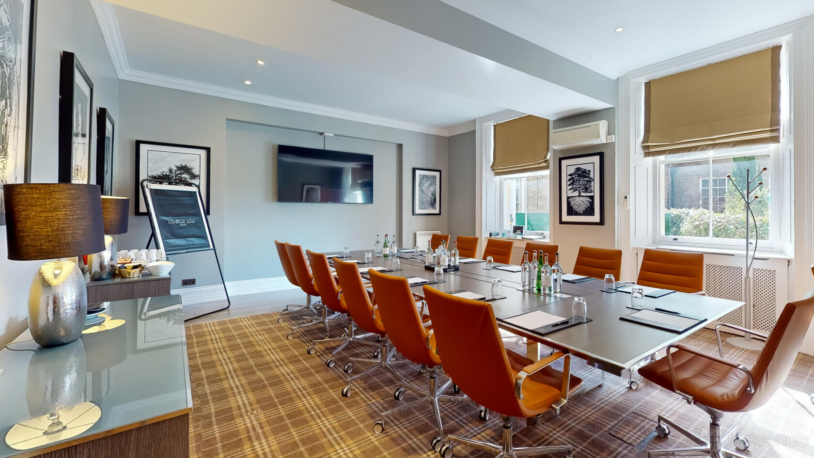 A hotel boardroom with orange leather chairs, large screen, flipchart, and natural light at Oatlands Park Hotel Cedar Room.
