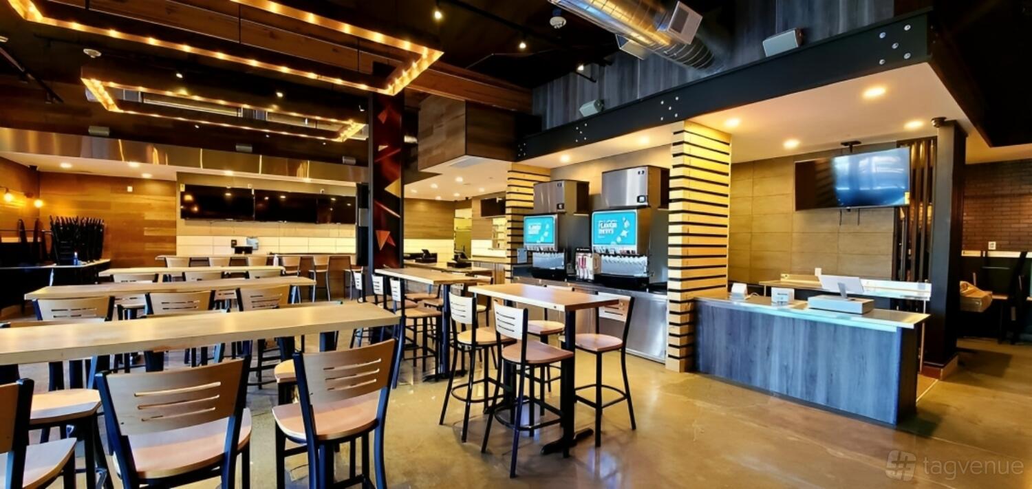 A restaurant dining area with wooden tables, high chairs, exposed ductwork, and a self-serve drink station at Fire Wings.