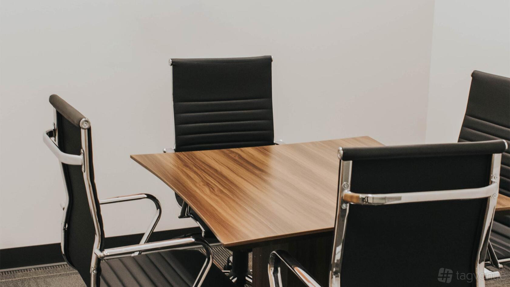 A meeting room with a wooden table and black leather chairs at Executive Workspace Park Ventura.