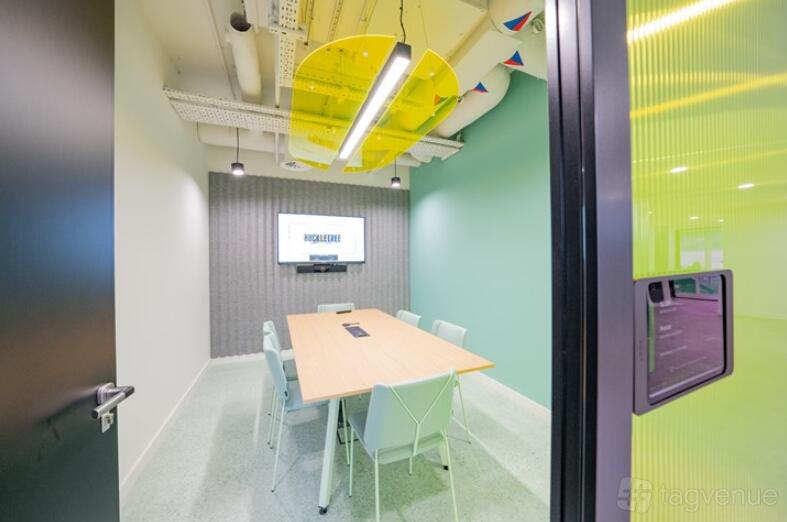 A meeting room with pastel chairs, a wall-mounted screen, and exposed ceiling pipes at Huckletree Oxford Circus.