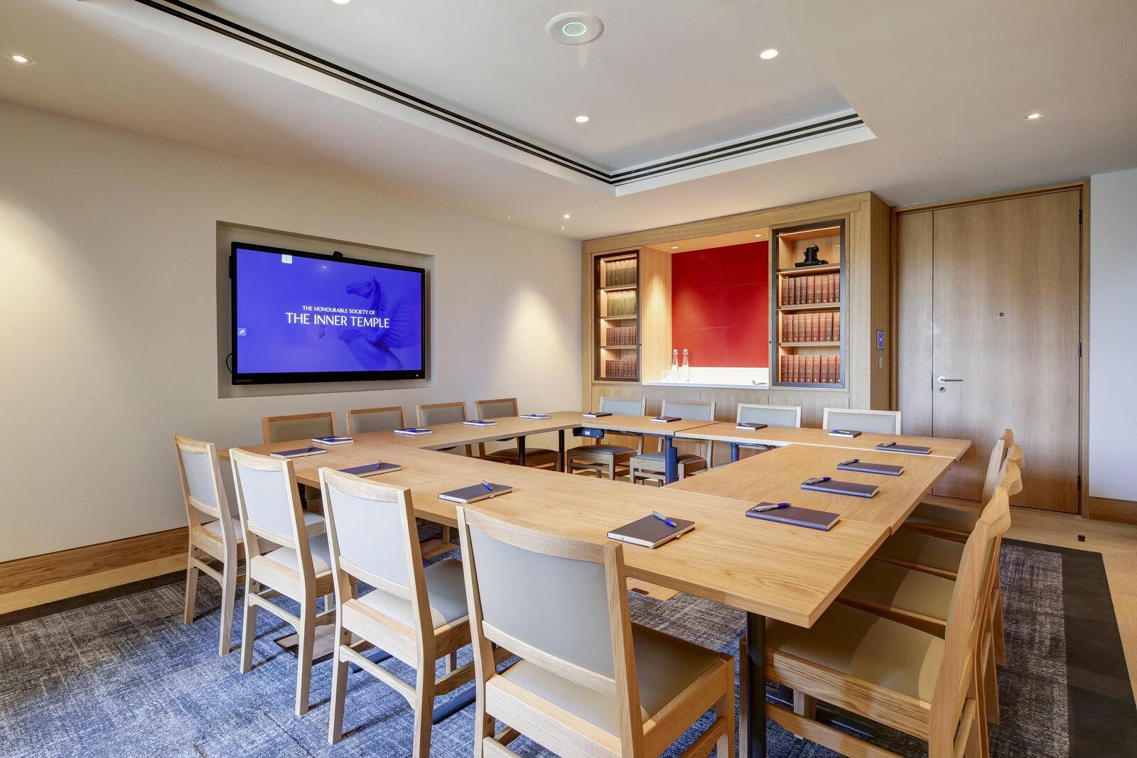 A meeting room with a U-shaped wooden table, cream chairs, built-in bookshelves, and a wall-mounted screen at The Inner Temple.