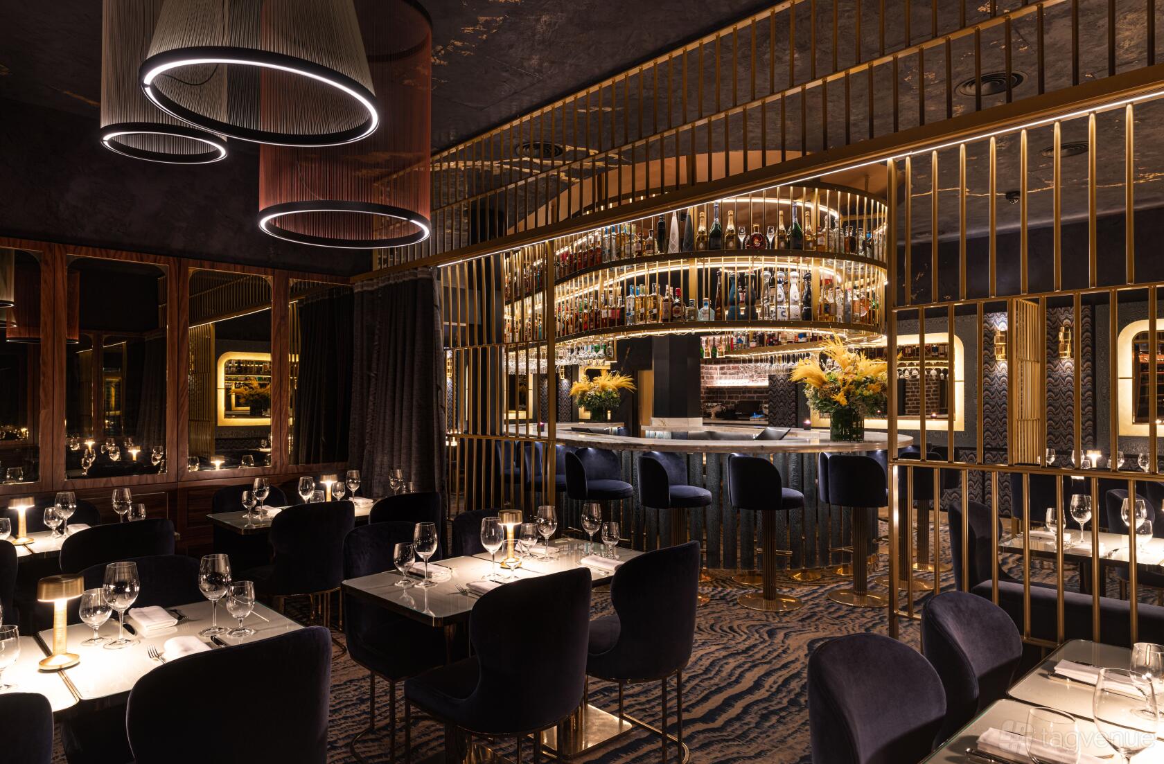 A restaurant with velvet chairs, round pendant lights, and a mirrored bar with gold accents at MAYA Manchester.