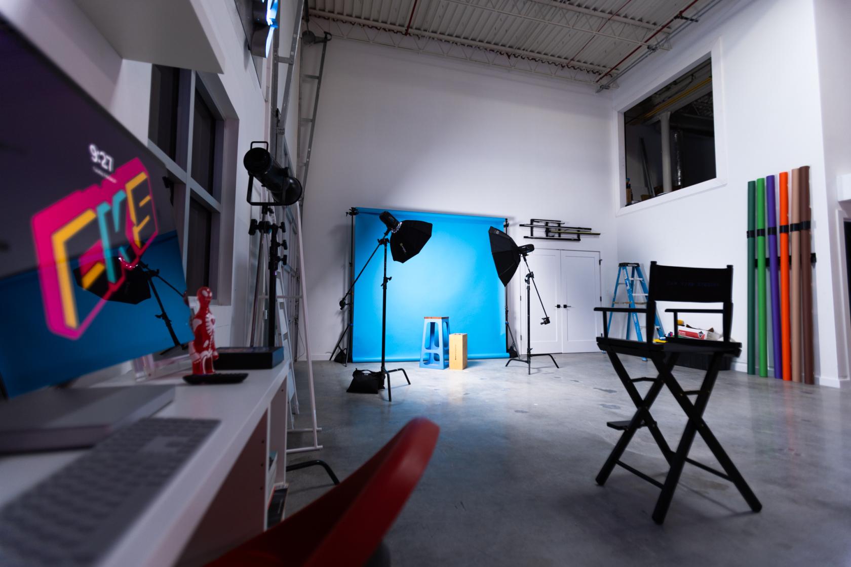A photo studio with a blue backdrop, softbox lights, director’s chair, and colorful props at Cam Kirk Studios.