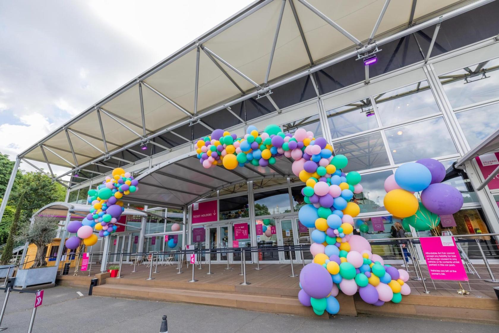 An event venue with a large glass entrance and a colorful balloon arch at Evolution London.