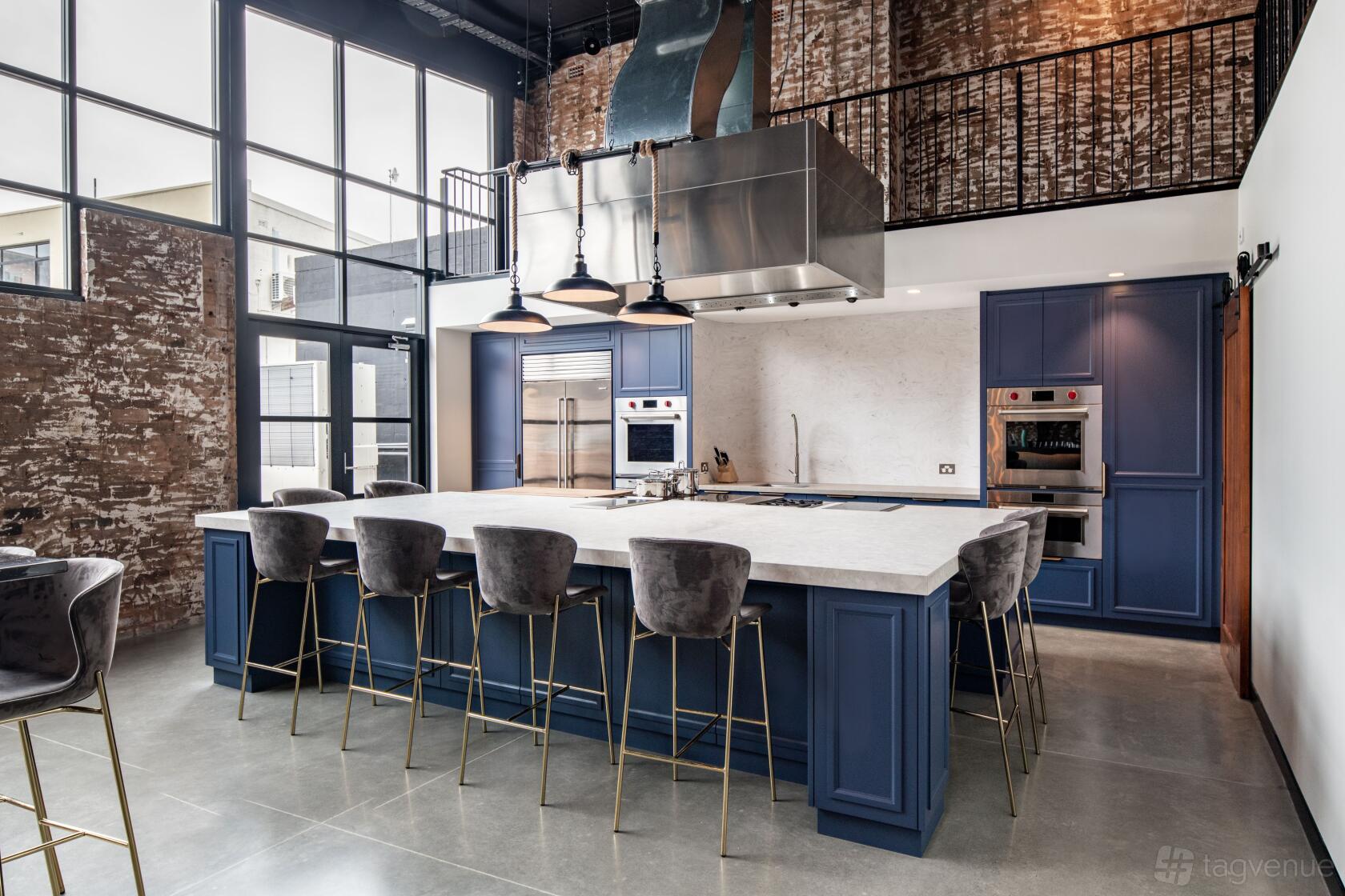 A photo studio with a large kitchen island, velvet barstools, brick accent wall, and natural light at La Botanique.
