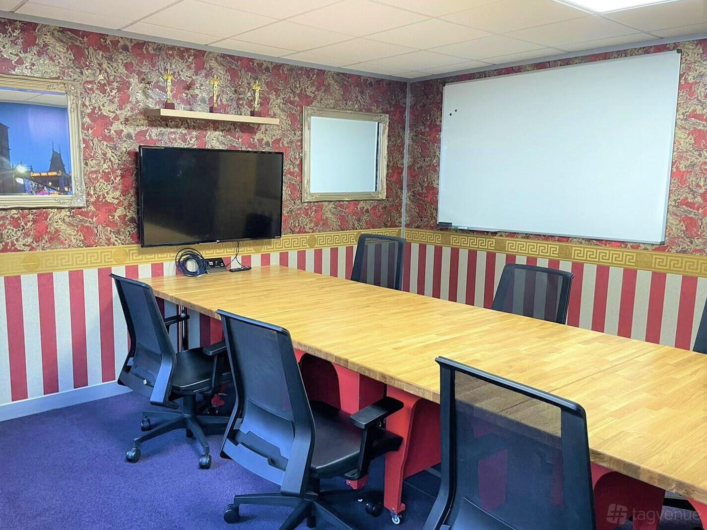 A meeting room with a long wooden table, black chairs, wall-mounted TV, and a large whiteboard at DeskLodge House Bristol.