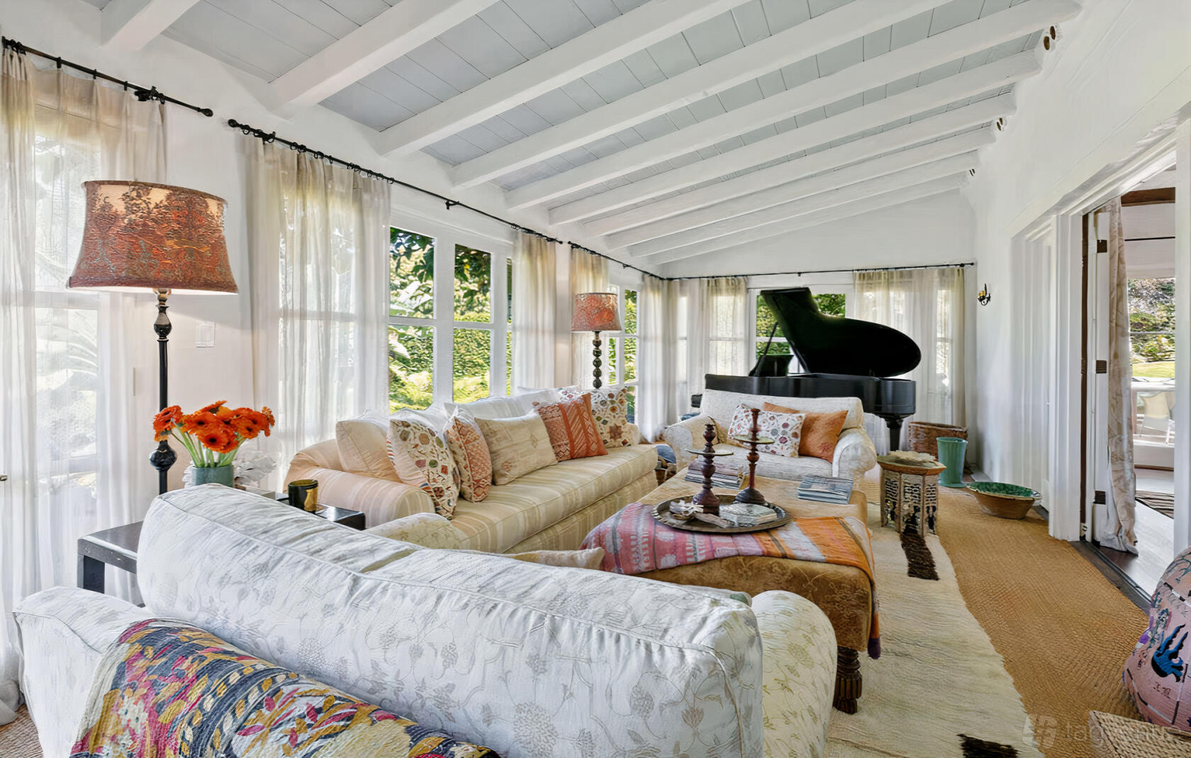 A house with exposed beam ceilings, floral sofas, a grand piano, and large windows at Ocean View Pool Estate.